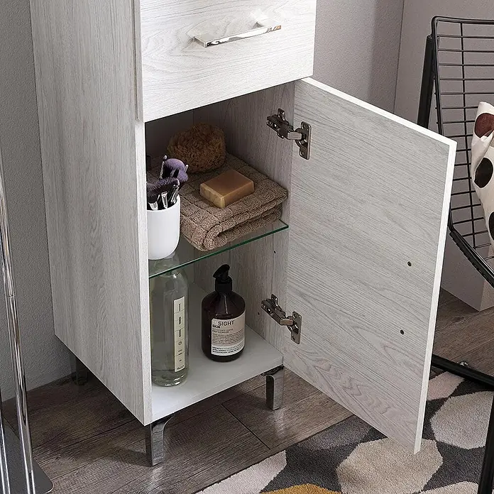 Kiamami Valentina Badmöbel-Set - Helles Holz - Hellgrauer Badschrank in Holzoptik mit Chromfüßen, offener Tür, Glasregal und Toilettenartikeln.