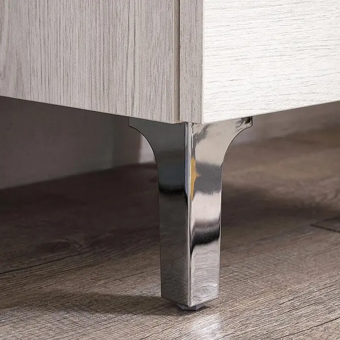 Kiamami Valentina Badmöbel-Set - Helles Holz - Modernes Chrombein stützt einen hellen Schrank mit Holzmaserung. Glatte, reflektierende Metalloberfläche.
