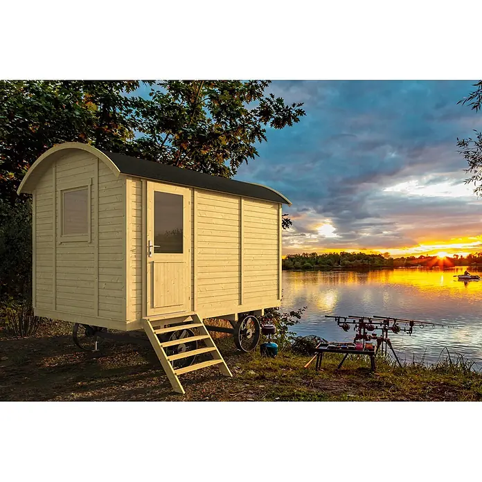 Tuindeco Gartenhaus Zirkuswagen Kerstin - Außenmaß inkl. Dachüberstand (B x T): 360 x 240 cm, Holz, Naturbraun - Helles Holzhäuschen auf Rädern an einem See bei Sonnenuntergang, mit Angelruten im Vordergrund.