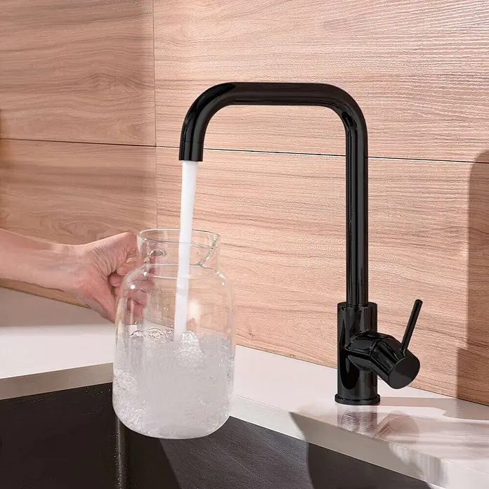 Poalgi Spültischarmatur Comfort - Kristallschwarz, Glänzend - Schwarze Küchenarmatur mit quadratischem Auslauf, Wasser läuft in ein Glasgefäß in einer modernen Küche.