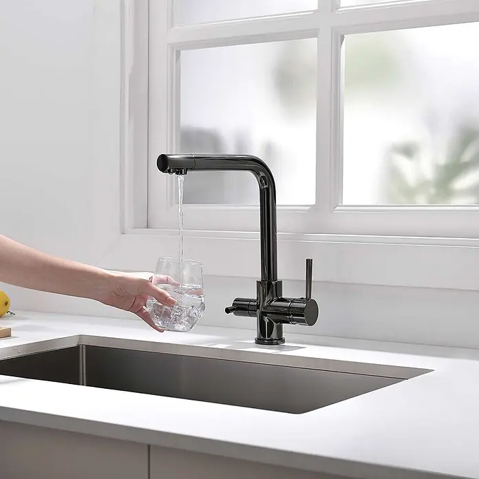 Poalgi Spültischarmatur Life - Kristallschwarz, Glänzend - Schwarze Küchenarmatur im eckigen Design spendet Wasser in ein Glas über einer dunklen Spüle.