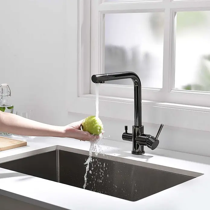 Poalgi Spültischarmatur Life - Kristallschwarz, Glänzend - Glänzender dunkler Küchenhahn mit Ausziehbrause, wäscht grünes Obst in einem schwarzen Spülbecken.