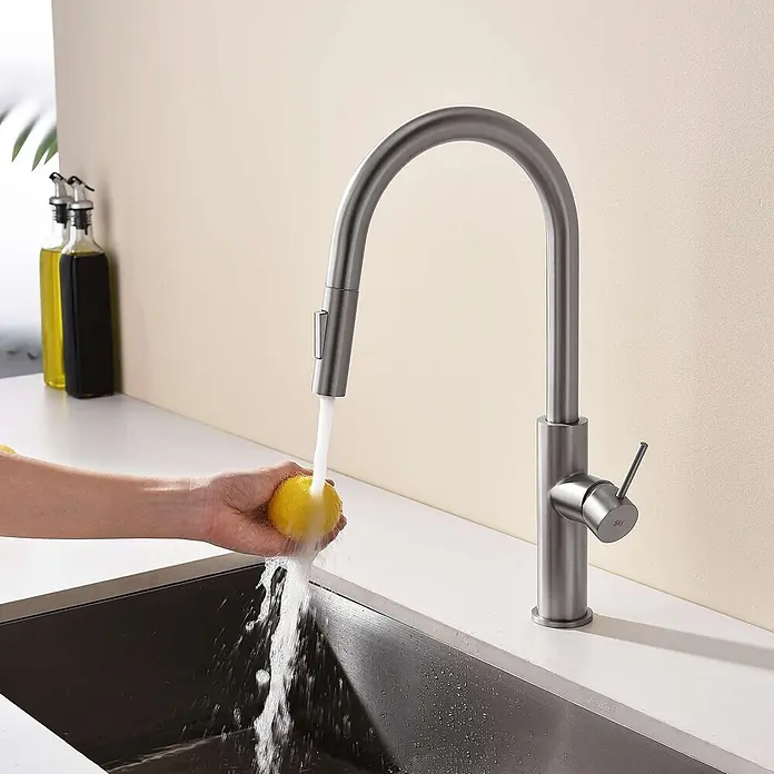 Poalgi Spültischarmatur River - Nickel, Seidenmatt - Gebürstete Metall-Küchenarmatur mit hohem Auslauf, die eine Zitrone unter fließendem Wasser im Spülbecken wäscht.