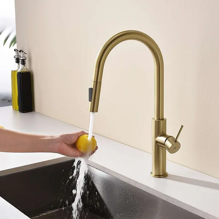Poalgi Spültischarmatur River - Goldfarben, Seidenmatt - Goldene Küchenarmatur mit herausziehbarem Brausekopf, der Wasser auf eine Zitrone in einer schwarzen Spüle laufen lässt.
