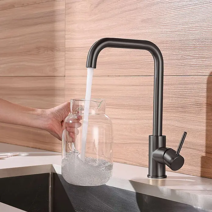 Poalgi Spültischarmatur Comfort - Gun Metal, Seidenmatt - Mattschwarze Küchenarmatur füllt eine Glaskanne mit Wasser in einer modernen Küche.