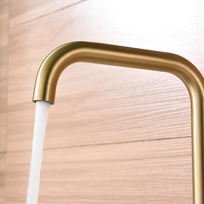 Poalgi Spültischarmatur Comfort - Goldfarben, Seidenmatt - Moderner Wasserhahn in gebürstetem Gold mit fließendem Wasser vor einer hellen Holzwand.