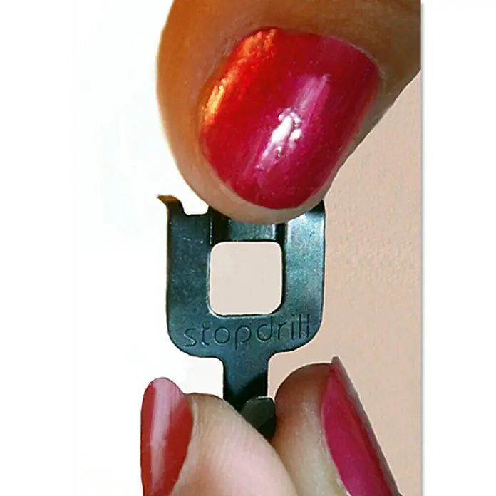 Fischer Gancho para colgar cuadros Stopdrill - Carga soportada: 8 kg, 8 ud., Metal, Plateado - Primer plano de una herramienta Stopdrill sostenida en las manos de una persona con las uñas pintadas de rojo.