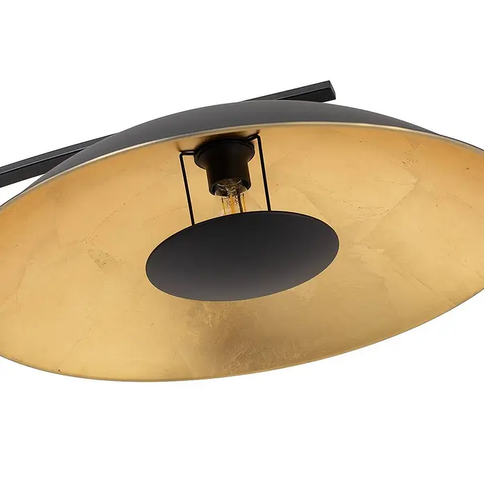 Lindby Stehleuchte Emilienne - schwarz, schwarz, E27 - Nahaufnahme einer schwarzen Lampe mit goldener Innenseite und sichtbarer Glühbirne, von einem schwarzen Arm getragen.