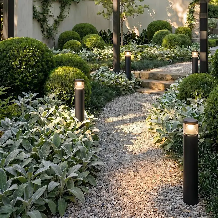Lucande Außenlaterne Darja -  - Schwarze zylindrische Pollerleuchten erhellen einen Kiesgartenweg inmitten üppigen Grüns.