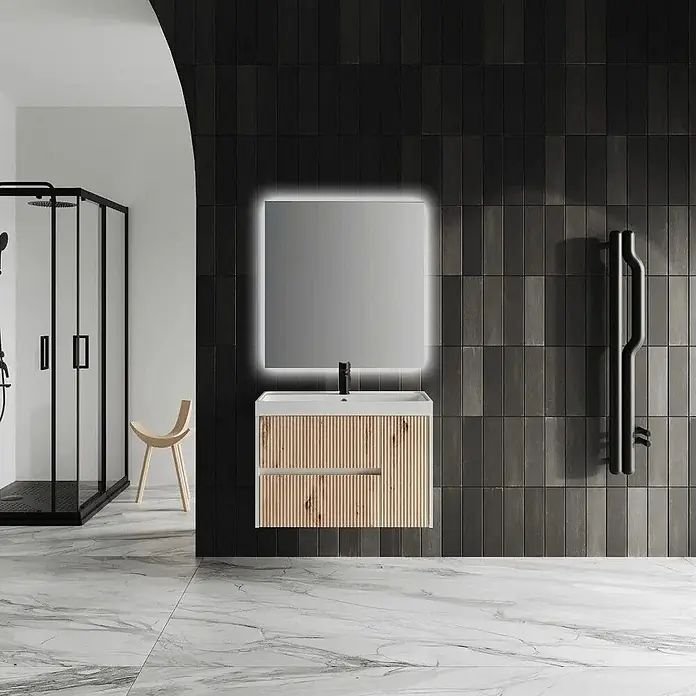Kiamami Valentina Badmöbel-Set - Braun - Moderner Badwaschtisch mit geriffelter heller Holzfront, weißem Waschbecken, schwarzem Wasserhahn und beleuchtetem Spiegel an dunkler Fliesenwand.