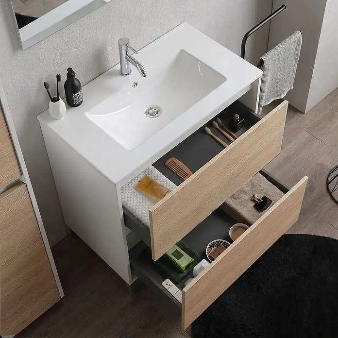Kiamami Valentina Badmöbel-Set - Helles Holz - Weißer Badezimmer-Waschtisch mit integriertem Waschbecken und zwei offenen hellen Holzschubladen, gefüllt mit Toilettenartikeln.