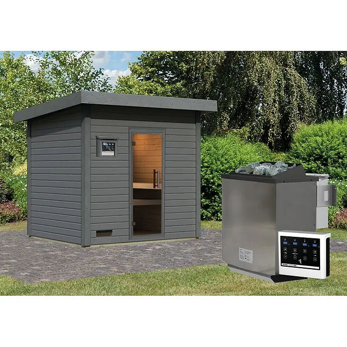 Karibu Saunahaus Kaapi 4 - 9 KW Bio-Ofen mit externer Steuerung, Anthrazit, L x B x H: 196 x 231 x 238 cm - Graue Außensaunakabine mit Glastür und externem Bedienfeld, neben einem freistehenden Saunaofen mit Steinen, auf einer Terrasse.