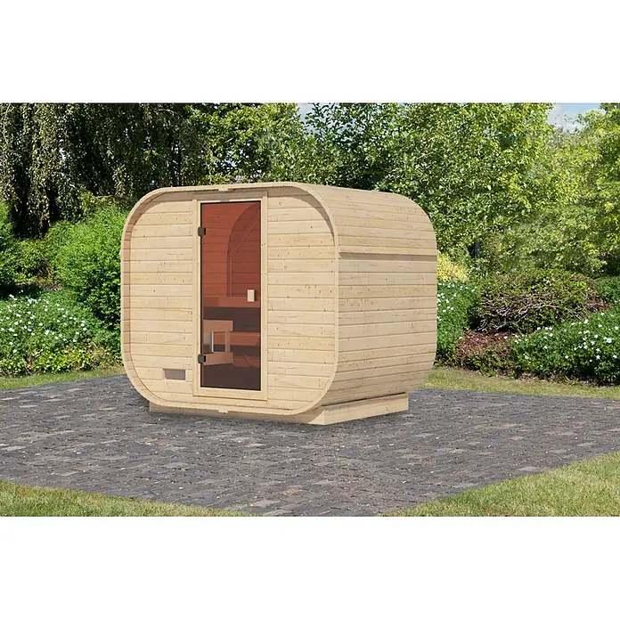 Karibu Saunahaus Quadro 1 Plus - Ohne Ofen, Natur, L x B x H: 385 x 225 x 205 cm - Hellholz-Fasssauna mit dunkler Glastür auf gepflastertem Bereich in einem üppigen Garten.