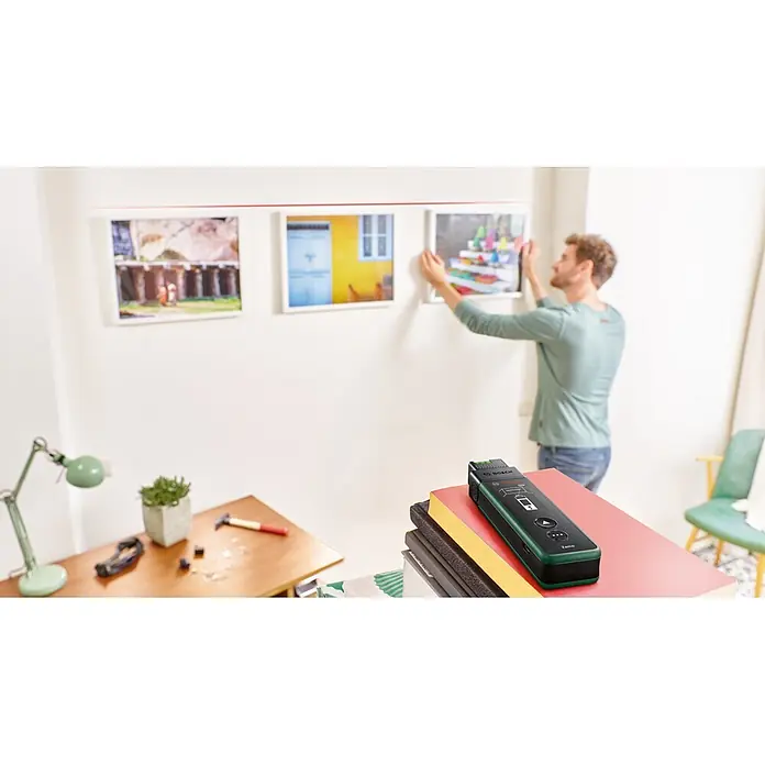 Bosch Laserentfernungsmesser Zamo Set - Messbereich: 0,15 - 40 m, 7 -tlg. - Bosch Zamo Laser-Entfernungsmesser, dunkelgrün und schwarz, auf Büchern, in einem Heimwerker-Umfeld.