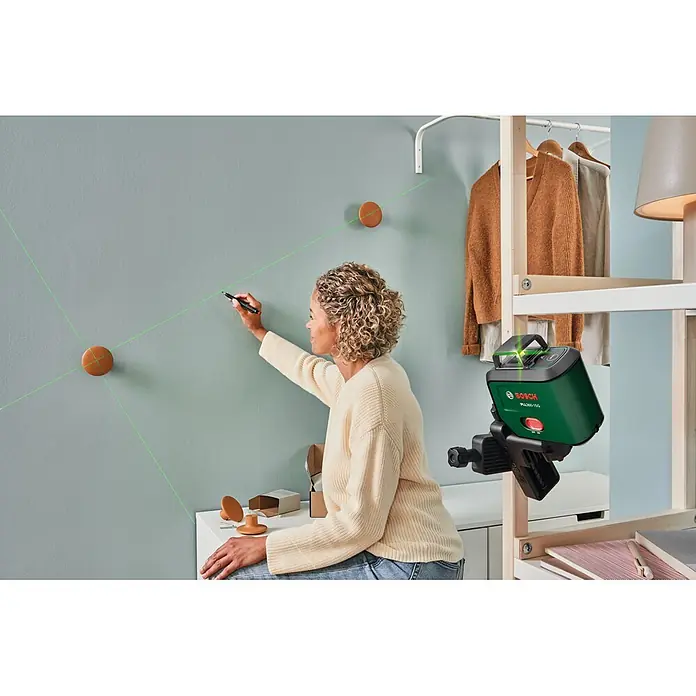 Bosch Kreuzlinienlaser PLL360-15G Premium Set - Max. Arbeitsbereich: 30 m, 3,6 V - Grünes Bosch PLL 360-1G Laser-Nivelliergerät projiziert grüne Linien an eine Wand, von einer Frau zum präzisen Anzeichnen genutzt.