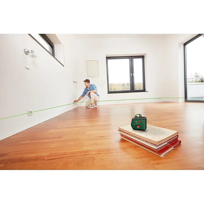 Bosch Kreuzlinienlaser PLL360-15G Set - Max. Arbeitsbereich: 30 m, 1 Akku, 3,6 V - Grünes Bosch Kreuzlinienlaser PLL 360-150 auf Büchern, projiziert eine Linie, die ein Mann an der Wand anzeichnet.