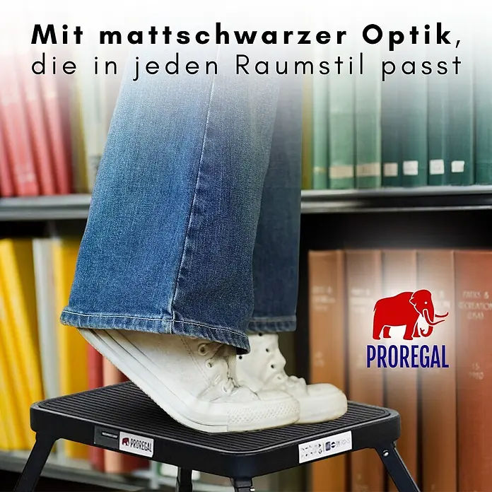 Proregal Klapptritt Tritthocker klappbar - Anzahl Tritte: 1 Stk., Belastbarkeit: 150 kg, Stahl - Eine Person steht auf einem mattschwarzen Trittschemel vor Bücherregalen.