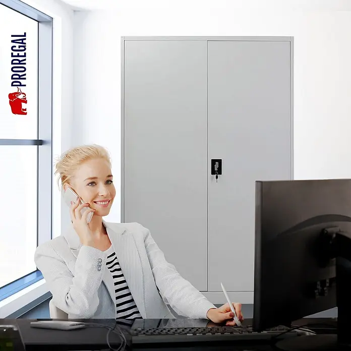 Proregal Aktenschrank Mega Deal 5x ELEPHANT komplett montiert - Lichtgrau - Hellgrauer Metallschrank im Büro, hinter einer Frau am Schreibtisch.