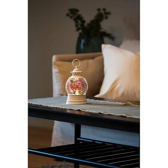 Konstsmide LED-Schneelaterne Schneemann mit Riesenrad - Innen, Weiß, 12,6 x 7,7 x 21 cm, Batteriebetrieben - Weiße Weihnachtsschneekugel-Laterne mit bunten Figuren auf einem dunklen Tisch.
