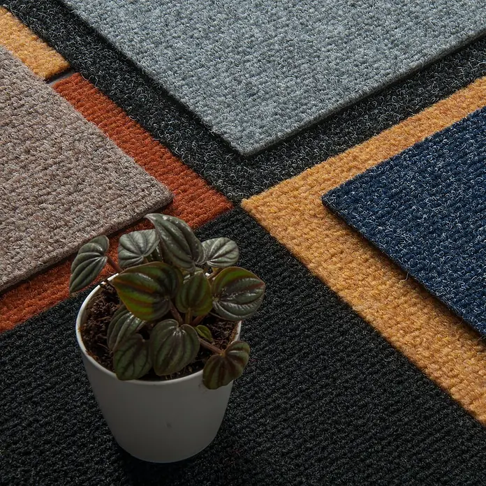 Bricoflor Teppichfliese - Breite: 50 cm, Nadelfilz, Polypropylen, schwarz - Texturierte Teppichfliesenmuster in Grau, Schwarz, Orange, Beige, Gelb und Blau, mit einer kleinen Pflanze.