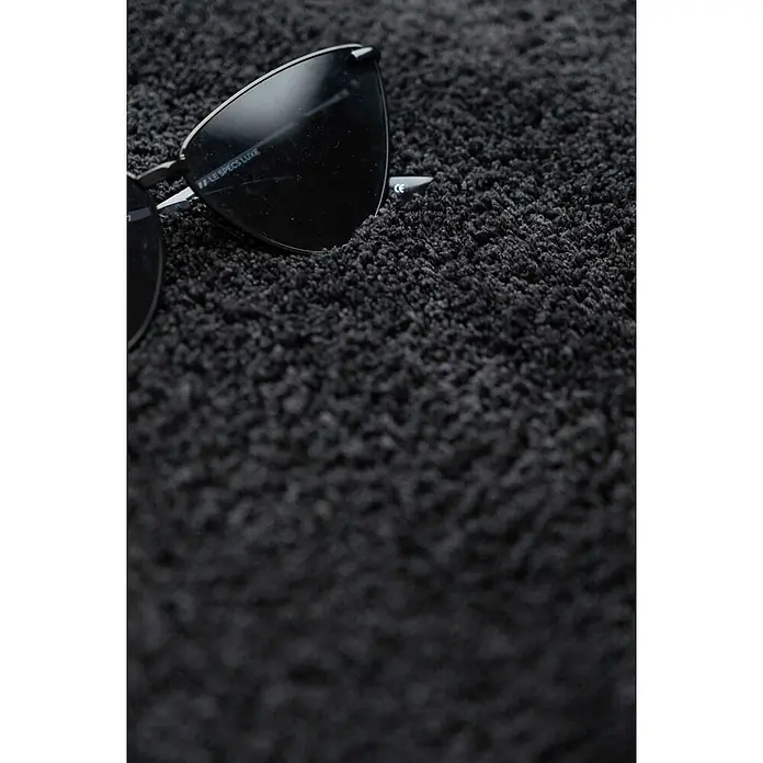 Bricoflor Teppichfliese - Breite: 50 cm, Velours, anthrazit - Schwarze Sonnenbrille mit dunklen Gläsern liegt auf einer dunklen, zotteligen Oberfläche.