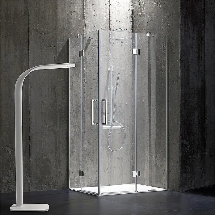 Kiamami Valentina Eckdusche - 900 x 700 x 1.900 cm, Transparent, Stärke: 6 mm - Moderne Glasduschkabine mit weißer Basis und Brausesystem, neben einer weißen Stehlampe.