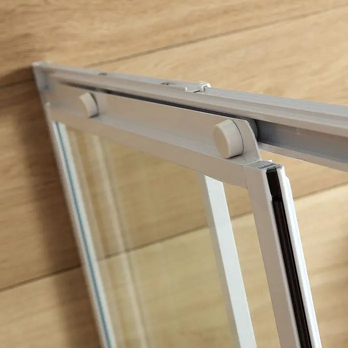 Kiamami Valentina Eckdusche - 90 x 90 x 185 cm, Transparent, Stärke: 6 mm - Nahaufnahme einer weiß gerahmten Glasschiebetür mit weißen Rollen vor Holz.