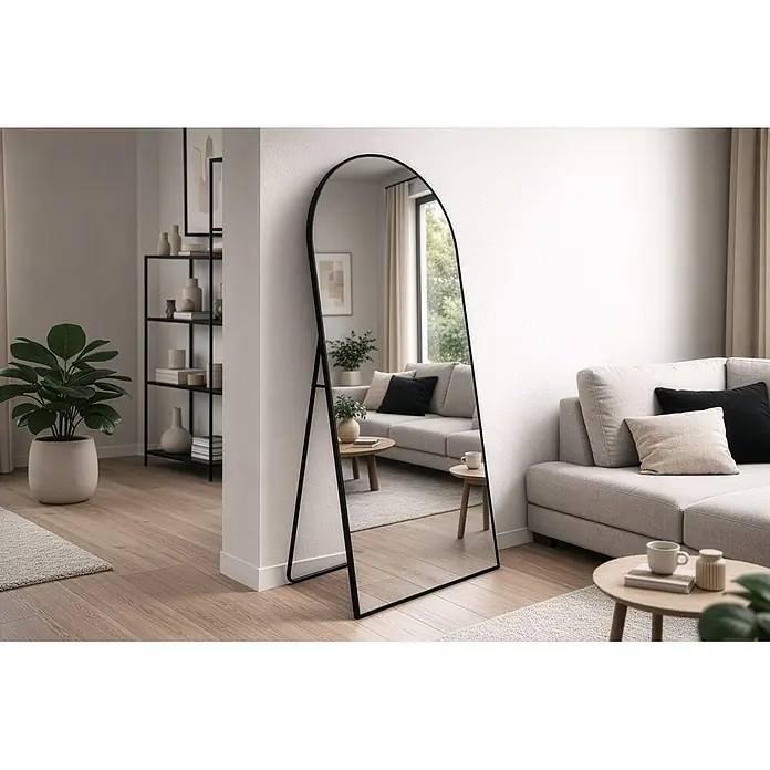 Standspiegel Mira - 70 x 170 cm, Gebogen, Schwarz - Gewölbter Ganzkörperspiegel mit schwarzem Rahmen lehnt im Wohnzimmer und reflektiert den Raum.