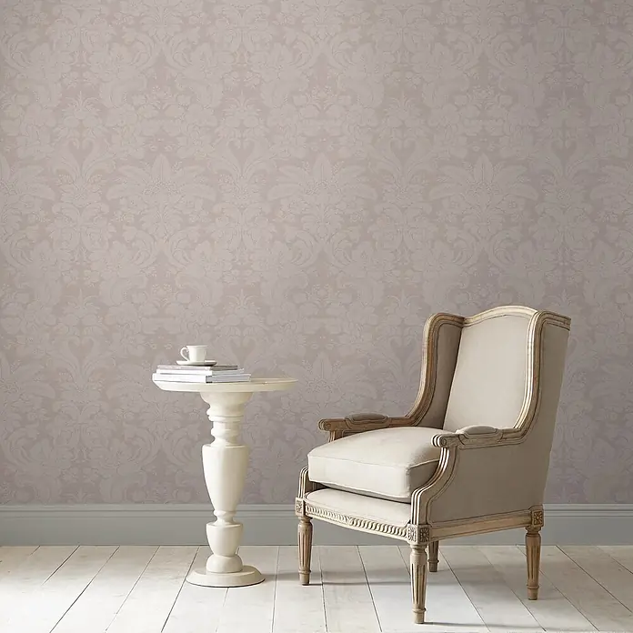 Laura Ashley Vliestapete Vliestapete Martigues Damast - Lila/Violett, Floral, 10 x 0,52 m - Helle taupefarbene Damasttapete mit dezentem Blumenmuster, bildet eine elegante Kulisse für einen beigefarbenen Stuhl und weißen Beistelltisch.