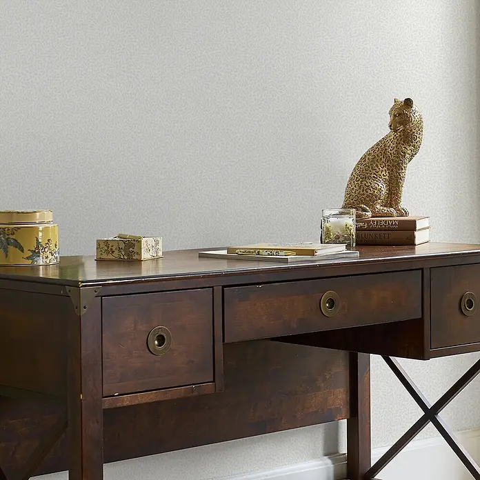 Laura Ashley Vliestapete Vliestapete überstreichbar kleine Weinreben - Weiß, Floral - Dunkler Holzschreibtisch mit Messingbeschlägen, dekoriert mit Leopardenstatue, Büchern und Zierkästen.