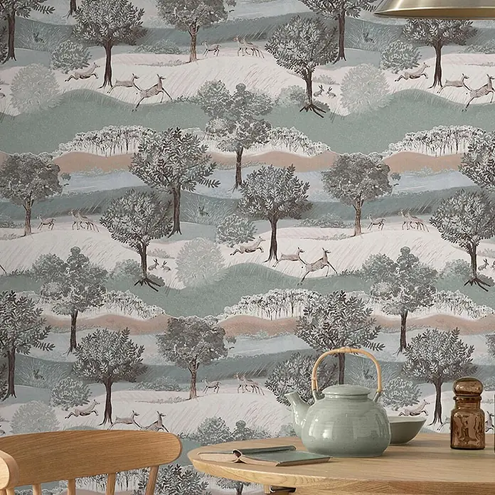 Laura Ashley Vliestapete Hartingdon - Grün, Ornament, 1.000 x 52 cm - Tapete mit einer stilisierten Waldszene mit Bäumen, Hügeln und Rehen, an einer Wand in einem Raum angebracht.