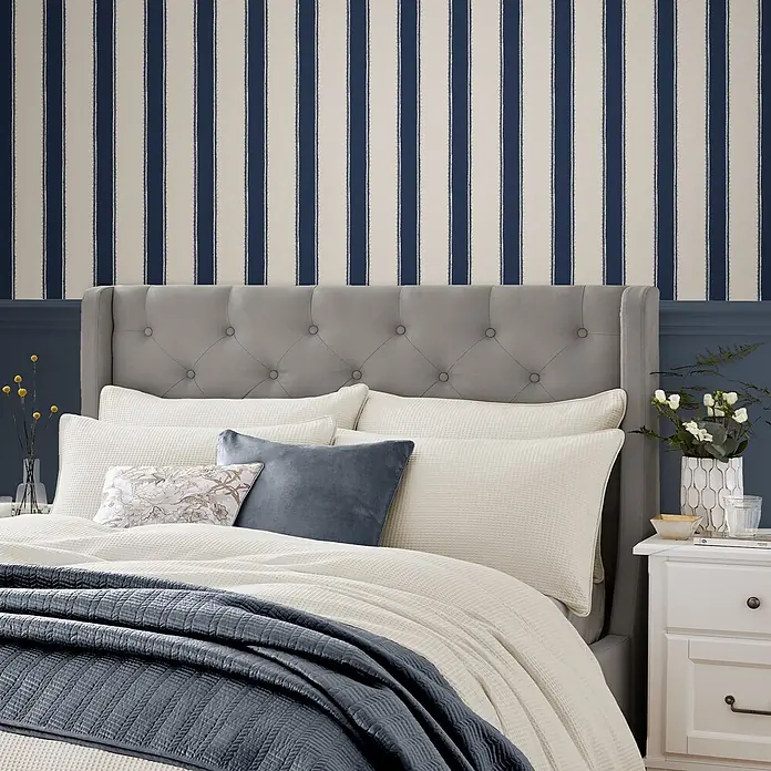 Laura Ashley Vliestapete Vliestapete Denwick - Blau, Ornament, 10 x 0,52 m - Creme-Waffelstrick-Bettwäsche mit marineblauer Steppdecke auf grauem, getuftetem Bett.