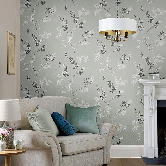 Laura Ashley Vliestapete Mari - Grün, Floral, 1.000 x 52 cm - Salbeigrüne Tapete mit zartem Muster aus grauen und weißen Blattranken, in einem gemütlichen Wohnzimmer mit Sofa und Kamin.