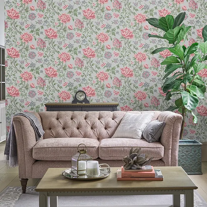 Laura Ashley Vliestapete Blumen - Grau, Floral, 1.000 x 52 cm - Rosa und graue Blumentapete im Wohnzimmer hinter einem rosafarbenen Sofa und Couchtisch, mit einer großen Pflanze.