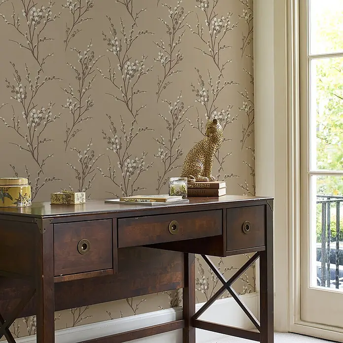 Laura Ashley Vliestapete Weidenkätzchen - Braun, Floral, 1.000 x 52 cm - Dunkler Holzschreibtisch mit Messingbeschlägen und gekreuzten Beinen in einer Raumeinrichtung.