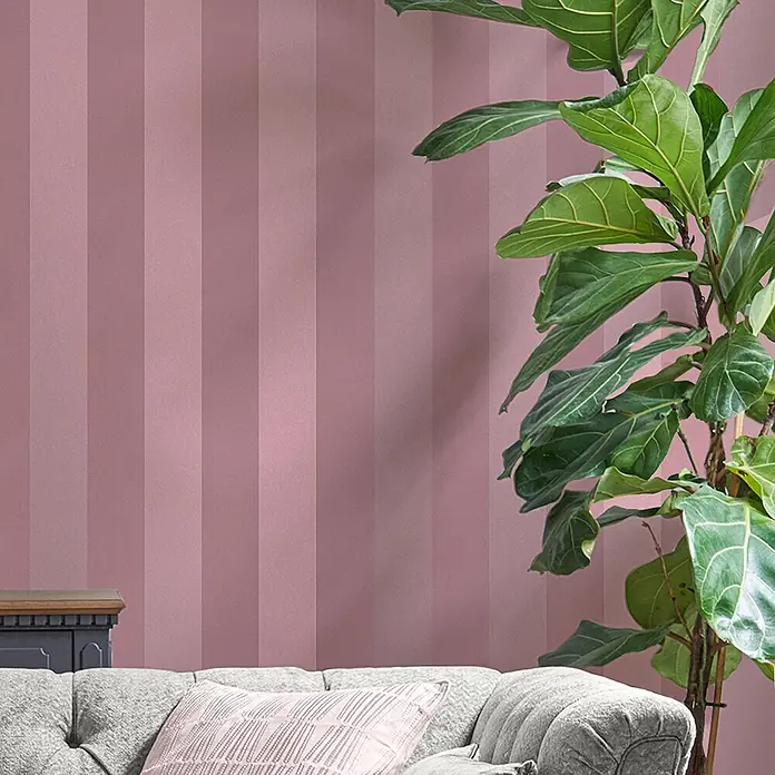 Laura Ashley Vliestapete Perlmuttstreifen - Rosa, Streifen, 1.000 x 52 cm - Rosa gestreifte Tapete in einem Wohnzimmer, hinter einem gemütlichen Sofa und einer großen Zimmerpflanze.