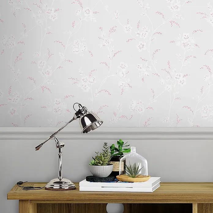 Laura Ashley Vliestapete Eva - Grau, Floral, 1.000 x 52 cm - Rosa und weißes Blumenmuster-Tapete auf hellgrauem Grund, an einer Wand über einem Holztisch.