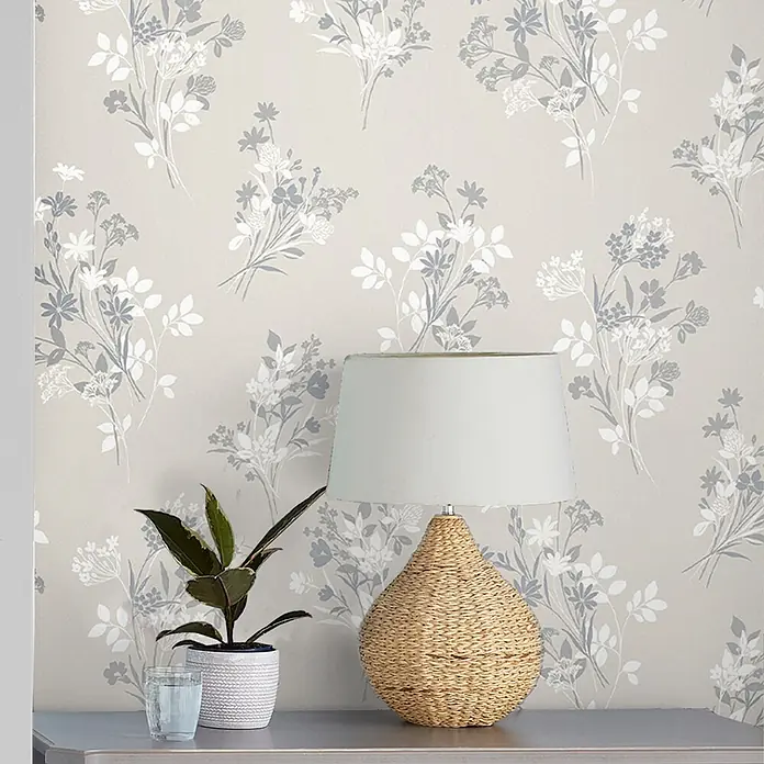 Laura Ashley Vliestapete Igerna Wiesenkerbel - Beige, Floral, 1.000 x 52 cm - Eine Tischlampe mit geflochtenem Naturfaserfuß und hellem Schirm steht auf einem Konsolentisch neben einer Pflanze.
