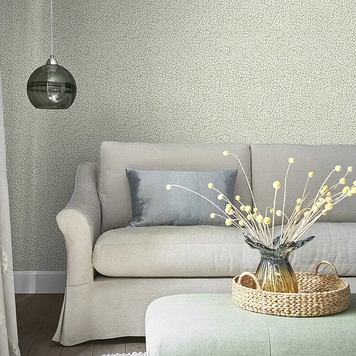 Laura Ashley Vliestapete Vliestapete Kleine Weinreben - Grün, Floral, 10 x 0,52 m - Hellgrüne Tapete mit zartem weißen Blättermuster, schmückt eine Wohnzimmerwand hinter einem neutralen Sofa.