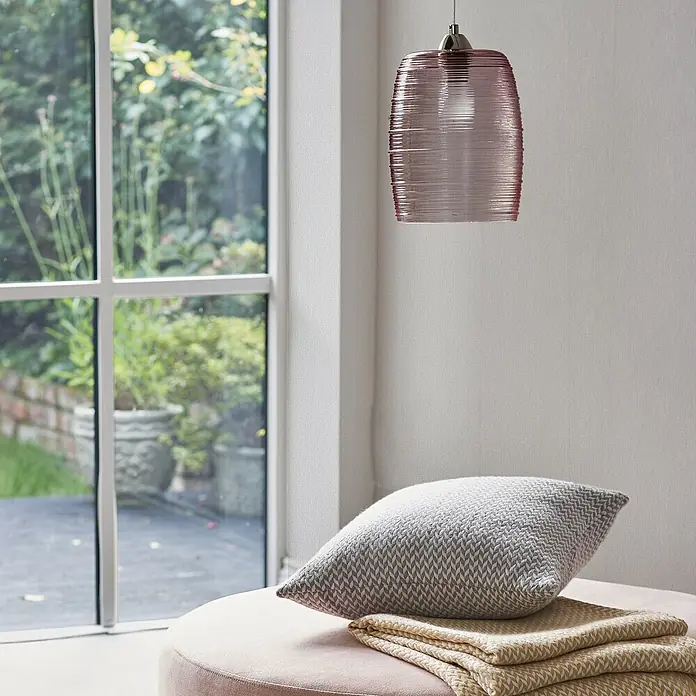 Laura Ashley Vliestapete Vliestapete überstreichbar - Weiß, Ornament - Rosa Pendelleuchte aus geripptem Glas hängt über grauem Kissen und gelbem Überwurf auf einem Hocker am Fenster.
