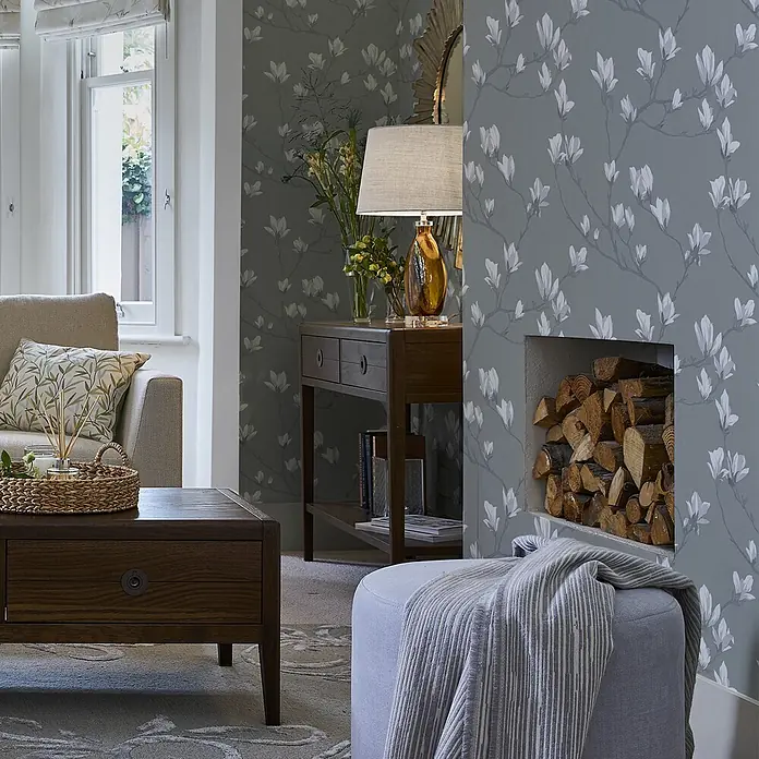 Laura Ashley Vliestapete Magnolienhain - Grau, Floral, 1.000 x 52 cm - Graue Tapete mit weißem Magnolienmuster in einem Wohnzimmer mit Holzmöbeln und hellem Sofa.