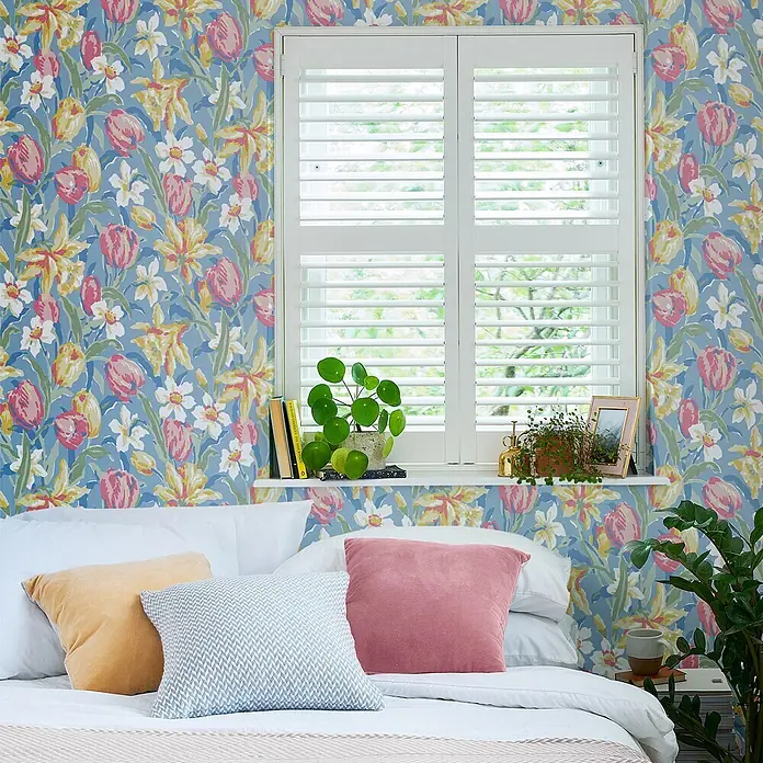 Laura Ashley Vliestapete Tulpen China - Blau, Floral, 1.000 x 52 cm - Blaue Blumentapete mit rosa Tulpen, gelben Narzissen und weißen Blumen an einer Schlafzimmerwand hinter Bett und Fensterläden.