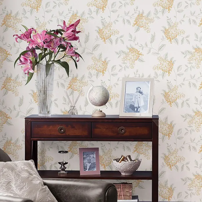 Laura Ashley Vliestapete Portland - Orange, Floral, 1.000 x 52 cm - Florale Mustertapete mit zarten hellgrünen Blättern und gelb-weißen Blütenbüscheln, die eine Wand im Wohnbereich schmückt.