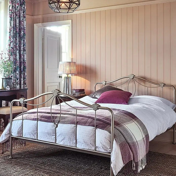 Laura Ashley Vliestapete Vliestapete Holzvertäfelung - Rosa, Streifen, 10 x 0,52 m - Ein messingfarbenes Metallbettgestell in einem gemütlichen Schlafzimmer, mit weißer Bettwäsche und lila Plaiddecke.