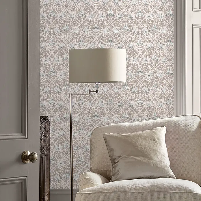 Laura Ashley Vliestapete Margam - Grau, Floral, 1.000 x 52 cm - Florale Tapete in Hellbraun- und Blautönen, die eine Wohnzimmerwand hinter einem cremefarbenen Sessel und einer Stehlampe schmückt.