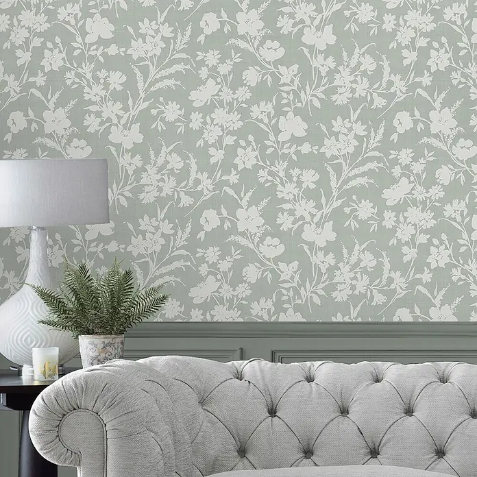 Laura Ashley Vliestapete Rye Blumen Monoprint - Grün, Floral, 1.000 x 52 cm - Salbeigrüntapete mit zarten weißen Blumen- und Pflanzenmustern an einer Wand, passend zu einem grauen Sofa und grüner Vertäfelung.