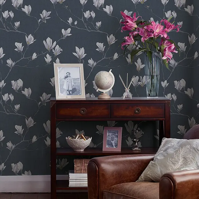 Laura Ashley Vliestapete Magnolienhain - Blau, Floral, 1.000 x 52 cm - Dunkelblaue Tapete mit zarten weißen und grauen Magnolienblüten und Ästen auf einer strukturierten Wand in gemütlichem Raum.