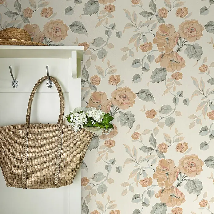 Laura Ashley Vliestapete Hibiskusblüten - Orange/Weiß, Floral, 1.000 x 52 cm - Gewebte Stroh-Einkaufstasche mit weißen Blumen an einer weißen Garderobe, ein Strohhut auf dem Regal darüber.