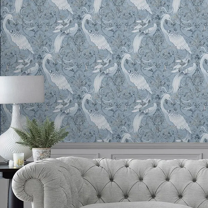 Laura Ashley Vliestapete Tregaron - Blau, Tieroptik, 1.000 x 52 cm - Blau gemusterte Tapete mit weißen Vögeln und Ornamenten an einer Wand über einem Sofa.