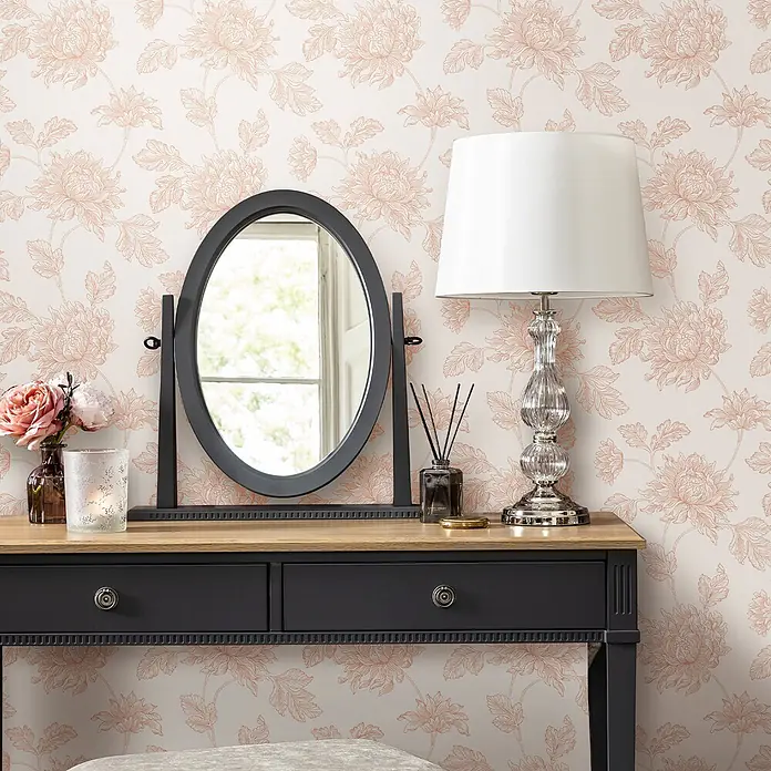Laura Ashley Vliestapete Vliestapete Stratton - Rosa, Floral, 10 x 0,52 m - Schwarzer Schminktisch mit Holzplatte und Spiegel, dekoriert mit Lampe und Blumen, vor floraler Tapete.